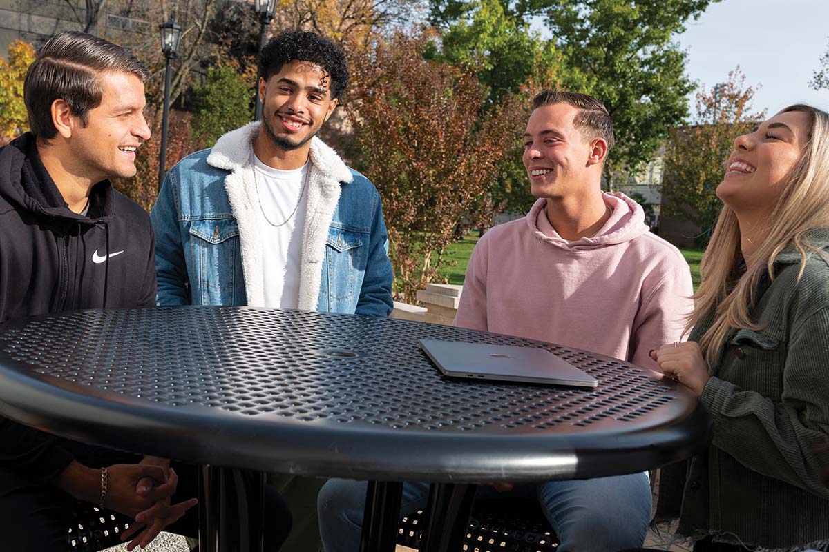Group of diverse students sitting around a table outside and laughing