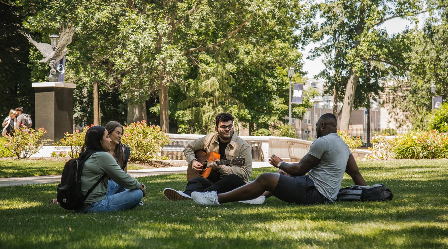 Students sitting in grass in circle with guitar