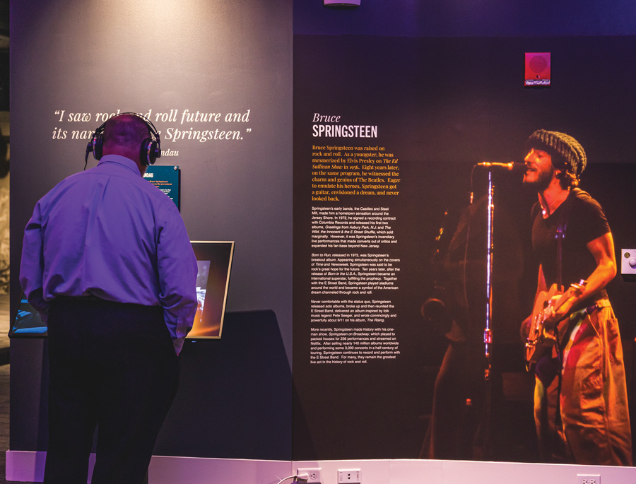 man wearing headphones and watching a screen at a Bruce Springsteen exhibit