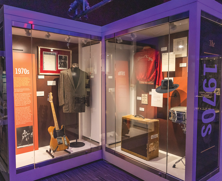 guitar, amplifier, snare drum, two jackets, and a hat behind glass in a Bruce Springsteen exhibit