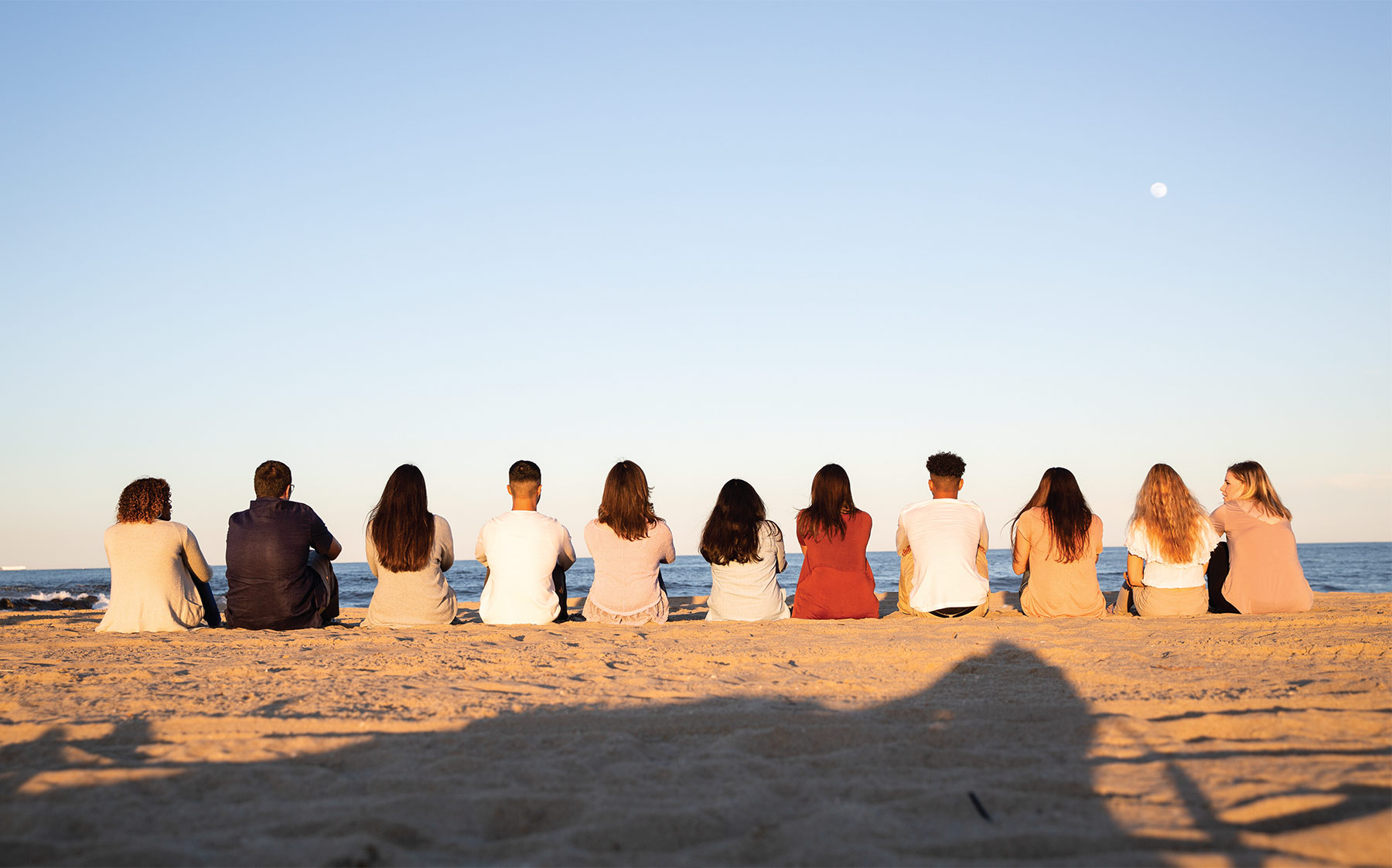 Monmouth University students sit on the sand next to each other at the beach