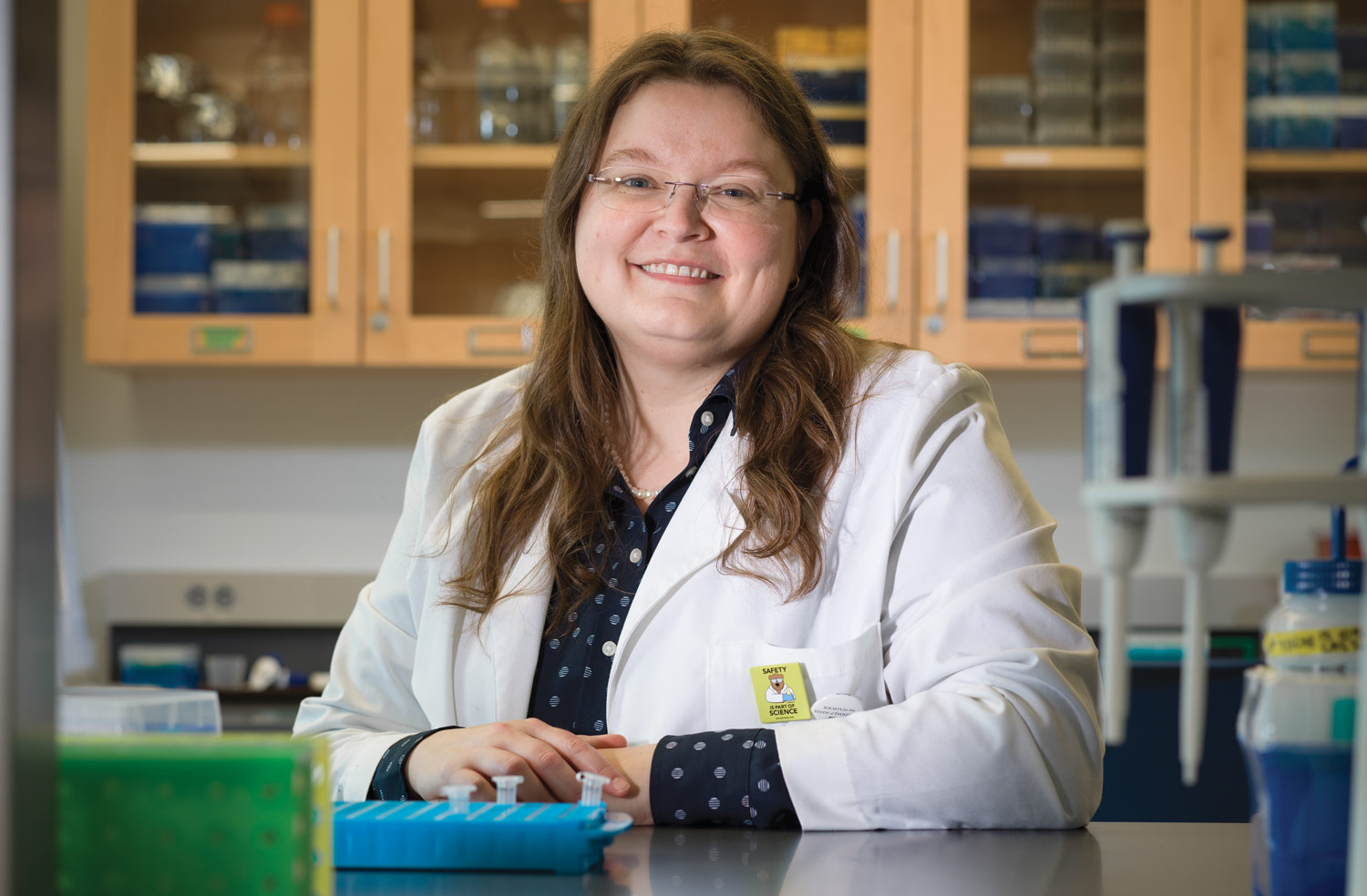 Megan Phifer-Rixey wearing a lab coat and smiling while standing in a lab