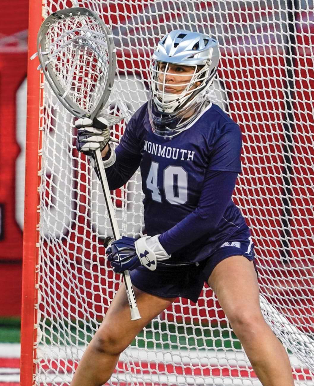 Monmouth Womens's Lacrosse player wears a mask and gloves while holding a goalie crosse and standing at the ready in the crease