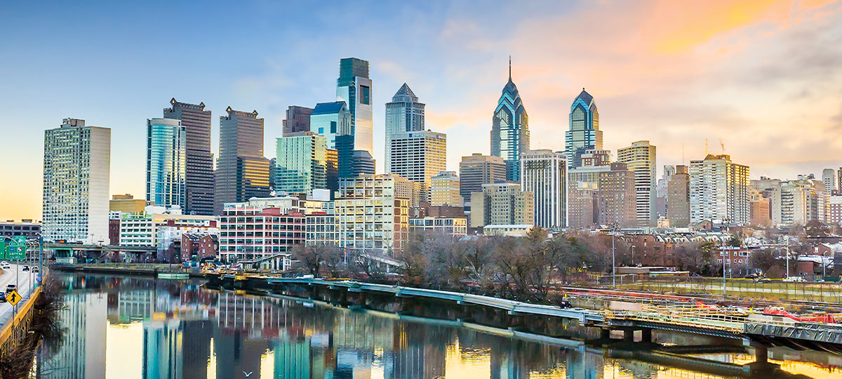 the Philadelphia skyline illuminated by a vibrant sunset, showcasing iconic buildings against a bright colorful sky