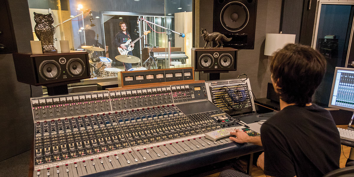 a student operates a mixer in a recording studio, surrounded by various audio equipment and soundproofing materials