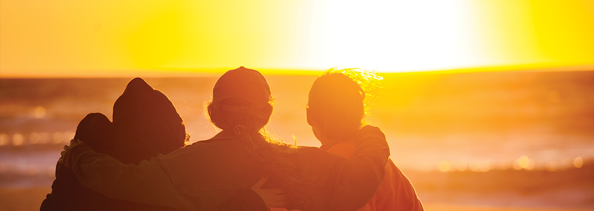 three individuals stand on the beach, silhouetted against a vibrant sunset