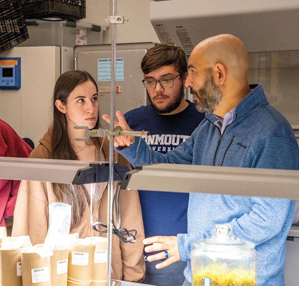 a professor stands at a lab lecturing to student standing close by